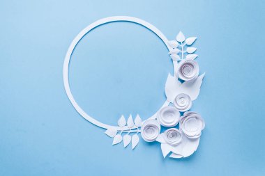 Yuvarlak çerçeve mavi zemin üzerine beyaz kağıt çiçeklerle. Kağıttan kesilmiş.