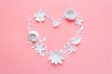 Beyaz kağıt çiçek, pembe bir arka plan üzerinde bir kalp şeklinde dizilmiş. Kağıttan kesilmiş.