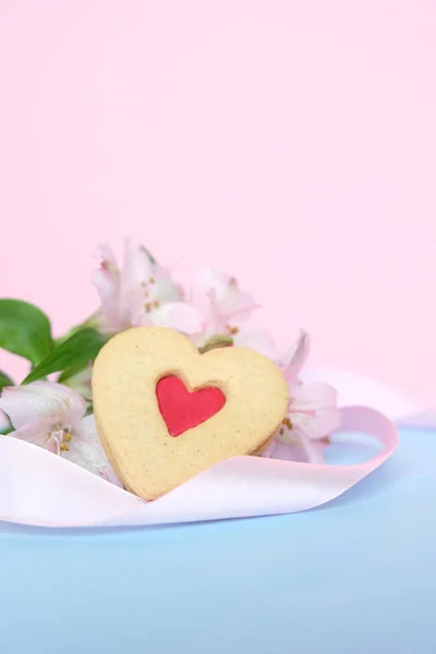 Biscoitos na forma de um coração com uma fita rosa em um fundo rosa com lisianthuses — Fotografia de Stock