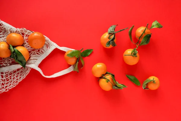 Composition with tangerines in a string bag on an red background — Stock Photo, Image