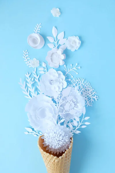 La mano sostiene un cono de gofre con flores de papel sobre fondo azul. Concepto de vacaciones . — Foto de Stock