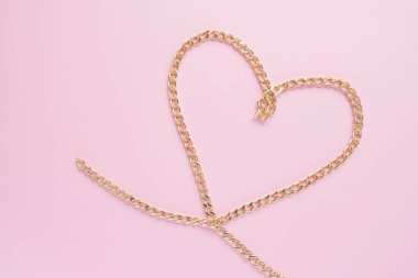 Pembe arka planda kalp şeklinde altın bir zincir serilmiş.