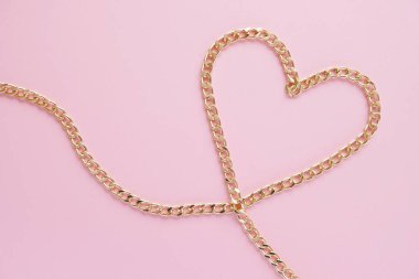 Pembe arka planda kalp şeklinde altın bir zincir serilmiş.