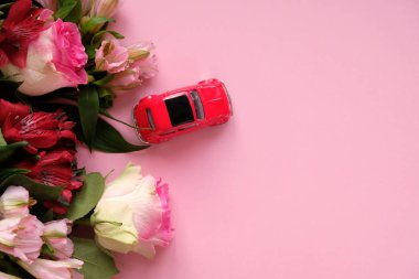 Küçük kırmızı oyuncak araba pembe arka planda bir buket pembe çiçek taşıyor..
