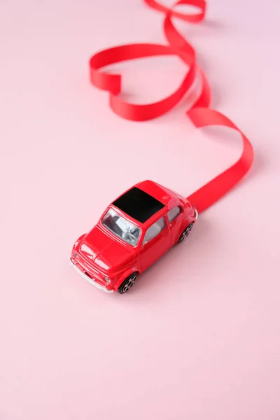 O brinquedo vermelho do carro carrega a fita de Valentine. Fita vermelha em forma de coração . — Fotografia de Stock