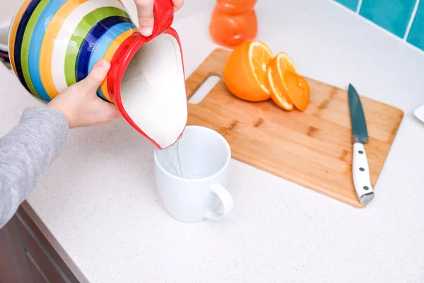 Der Junge Gießt Wasser Aus Einem Krug Einen Weißen Keramikbecher — Stockfoto