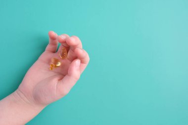Çocuğun elinde mavi arka planda bir doz vitamin var.