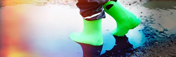 child with green rain boots jumps into a puddle