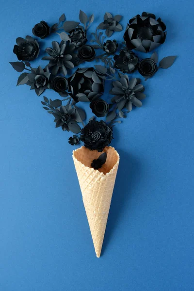 Waffle cone with black paper flowers on dark blue background. Holiday concept.
