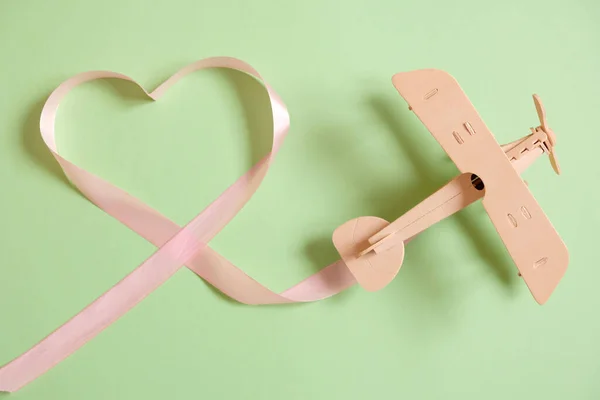 Houten speelgoed vliegtuig gelukkig met roze lint in de vorm van hart — Stockfoto