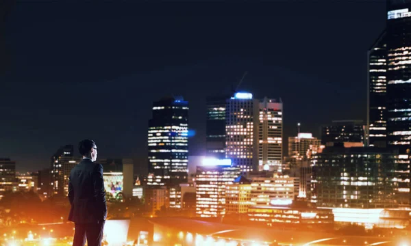 Businessman with suitcase looking at night city — Stock Photo, Image