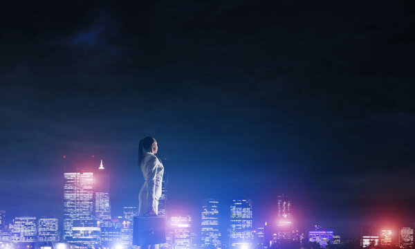 Rear view of elegant businesswoman viewing lights of night city. Woman looking at night city