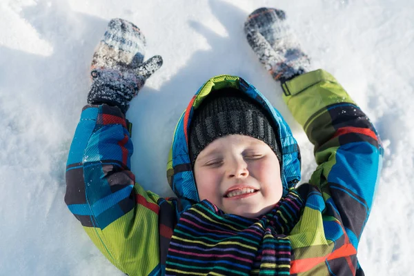 Χαριτωμένο αγόρι ξαπλωμένο στο χιόνι — Φωτογραφία Αρχείου