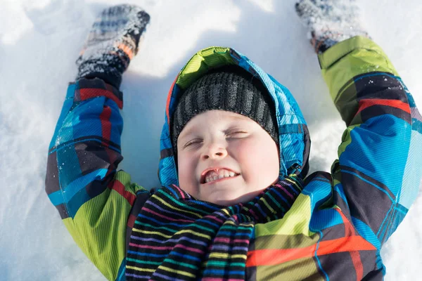 Menino bonito deitado na neve — Fotografia de Stock