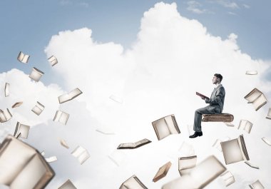 kitap üzerinde oturan genç işadamı