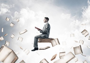 kitap üzerinde oturan genç işadamı