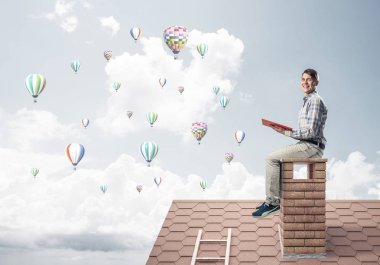 Kitap ile evin baca üzerinde oturan adam