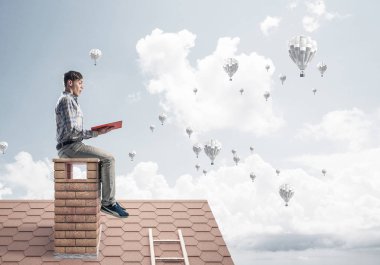 Kitap ile evin baca üzerinde oturan adam