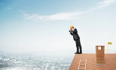 Young businessman in suit and helmet on roof  clipart
