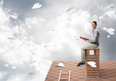 Kitap ile evin baca üzerinde oturan adam