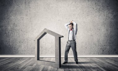 Öfkeli genç işadamı gürültüyle çarpmak ile eller taş ev simgesini boş beton odada olacak 