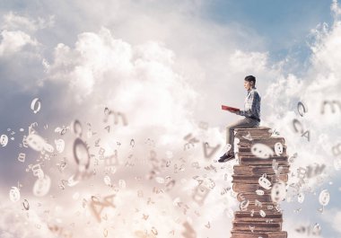 Genç işadamı kitap kitaplar ve etrafında uçan sembolleri yığını üzerinde otururken holding