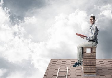 Kitap ile evin baca üzerinde oturan adam