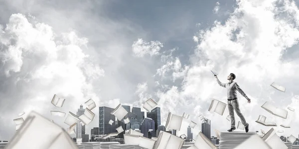 背景に空の Cloudly 本を飛行中に立っている間本を持つ手を追いついてカジュアルな服装での男 ミクスト メディア — ストック写真