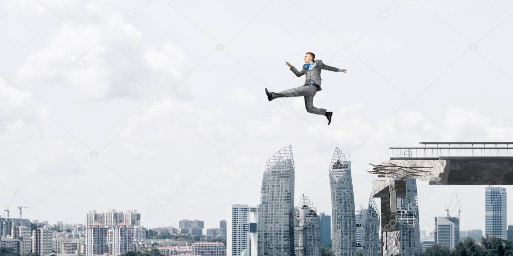 Businessman jumping over huge gap in concrete bridge as symbol of overcoming challenges with cityscape on background