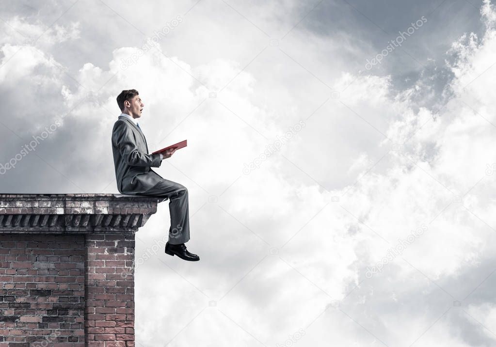 Young businessman sitting on building top