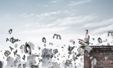 Elinde kırmızı kitap ile üst yapı üzerinde rahat oturan genç adam