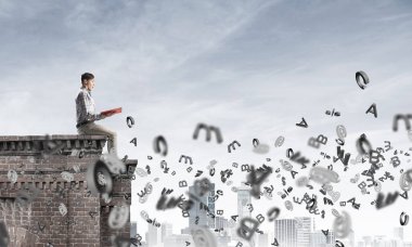 Elinde kırmızı kitap ile üst yapı üzerinde rahat oturan genç adam