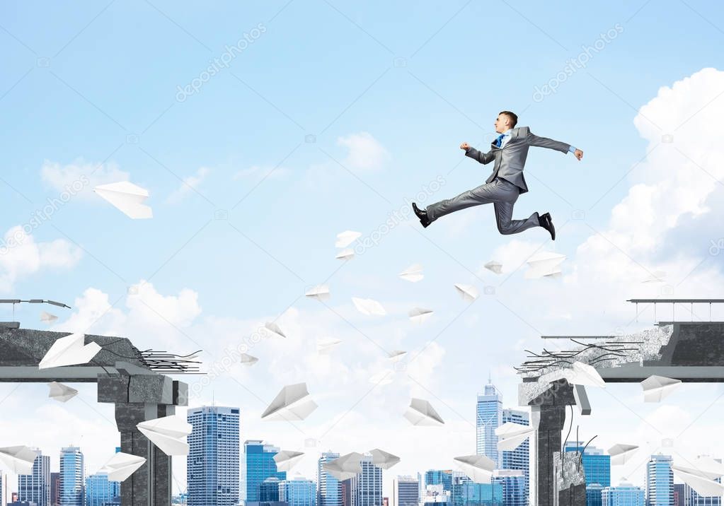 Businessman jumping over gap with flying paper planes in concrete bridge as symbol of overcoming challenges with cityscape on background, 3D rendering