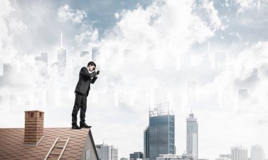 Çatıda duran ve dürbünle bakan bir iş adamı. Karıştırdı.