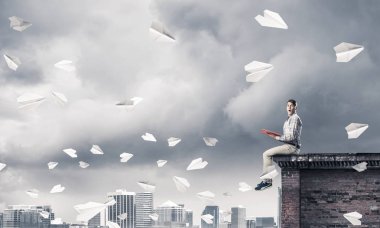 Elinde kırmızı kitap ile üst yapı üzerinde rahat oturan genç adam