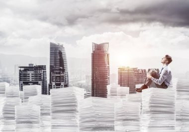 Düşünceli işadamı uzak belgeler cityscape ve arka plan üzerinde güneş ışığı ile yığını üzerinde otururken arıyorum. Karışık teknik.