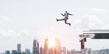 Cityscape arka plan üzerinde güçlüklerin üstesinden sembolü olarak büyük boşluğu beton köprü üstünden atlayarak işadamı