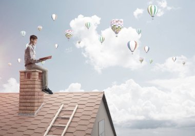 El ve havada uçan aerostats kırmızı kitap ile evin baca rahat oturan genç adam