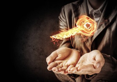 İşadamı yanan anahtar simgesi koyu arka plan duvara eliyle tutarak siyah elbiseli closeup.