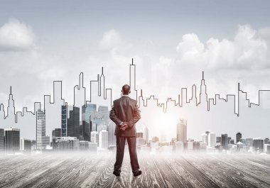 İşadamı arkasını dönüp modern iş merkezinin siluetine bakıyor.