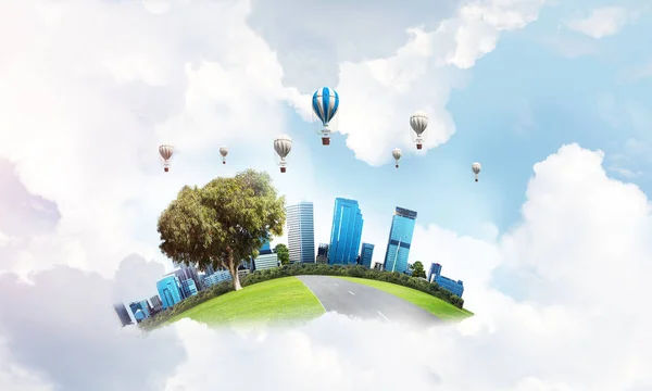 Green flying island with urban view of towers and skyscrapers. Flying aerostates and blue cloudy skyscape on background.