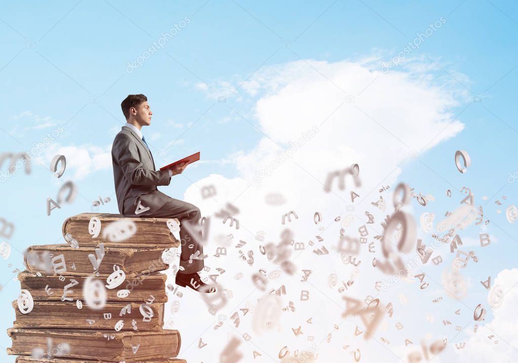 businessman sitting on pile of books 