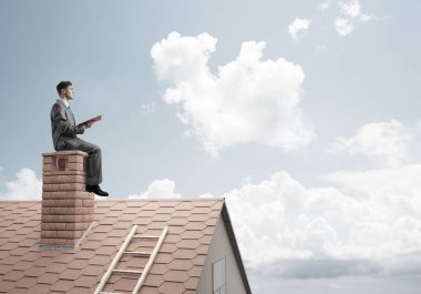 Elinde kırmızı kitap ile ev oturan takım elbiseli genç işadamı