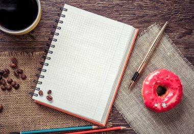 Açılmış not defteri ve bir fincan kahveyle ahşap masada çörek.