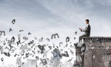 Elinde smartphone ile üst yapı üzerinde oturan genç işadamı