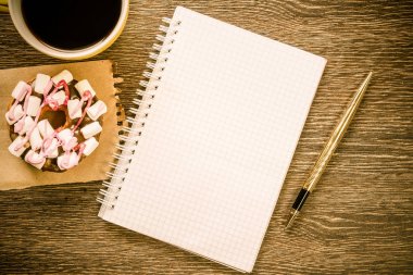 Açılmış not defteri ve bir fincan kahveyle ahşap masada çörek.