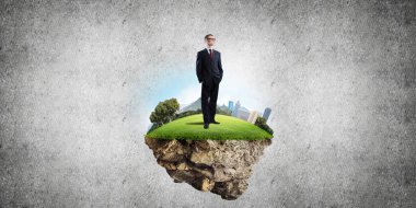 Yeşil yüzen adada beton zemine karşı duran kendine güvenen zarif iş adamı.