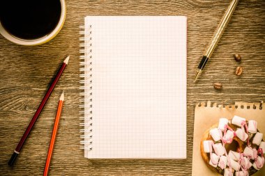 Açılmış not defteri ve bir fincan kahveyle ahşap masada çörek.