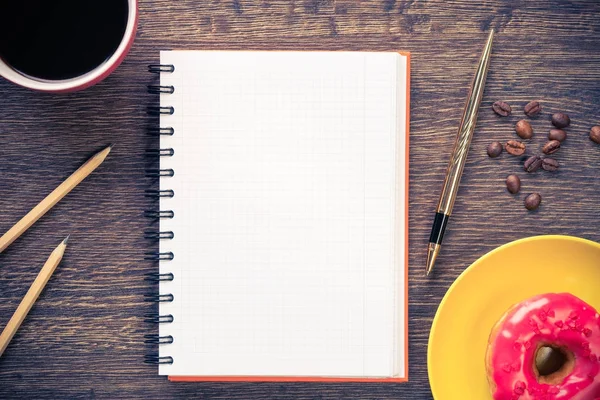 Açılmış not defteri ve bir fincan kahveyle ahşap masada çörek.