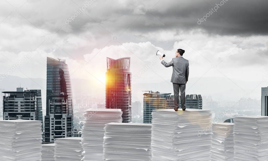 Businessman in suit standing on pile of documents